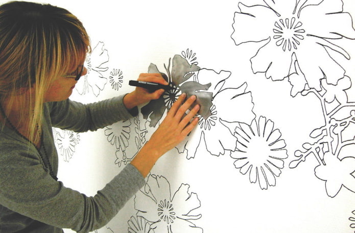 женщина рисует цветы на стене с помощью трафарета